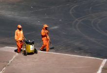 Dois trabalhadores de limpeza urbana atuam em uma rua de Brasília usando uniformes laranja.