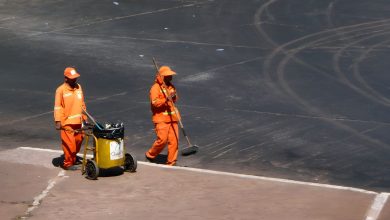 Dois trabalhadores de limpeza urbana atuam em uma rua de Brasília usando uniformes laranja.