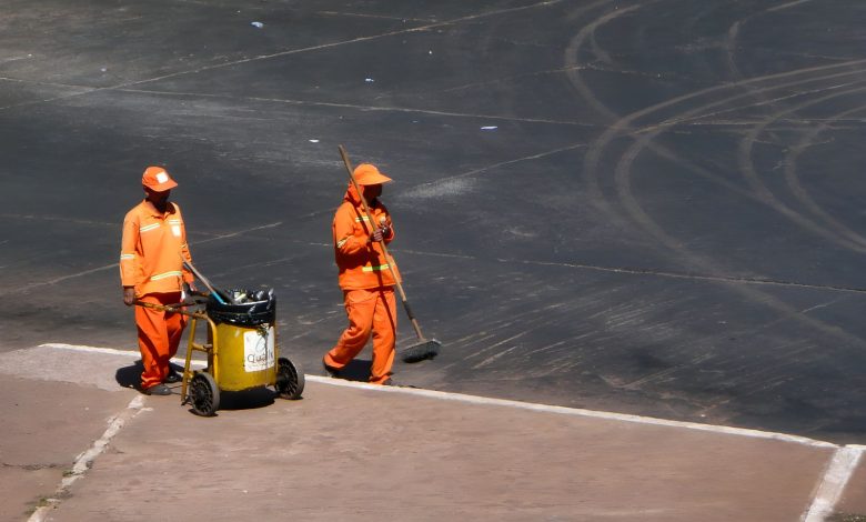 Dois trabalhadores de limpeza urbana atuam em uma rua de Brasília usando uniformes laranja.