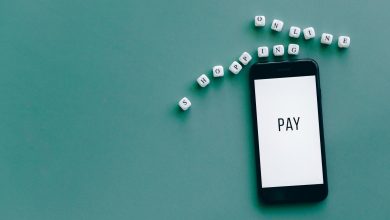 Smartphone com a palavra “PAY” cercado por dados com a expressão “online shopping”, sobre fundo azul-esverdeado.