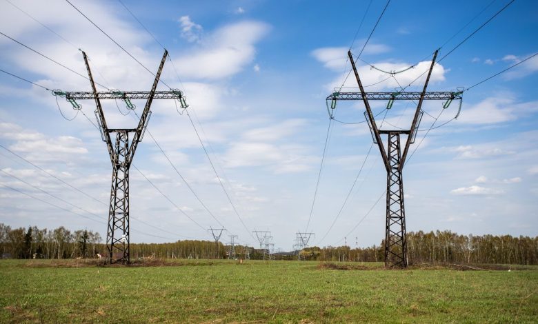 Linhas de transmissão de energia atravessam um campo verde sob céu azul com poucas nuvens.
