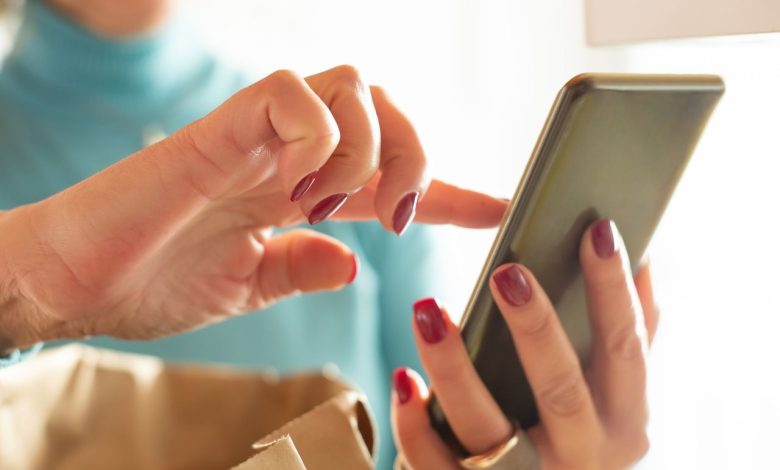 Mãos interagem com a tela de um smartphone em ambiente interno, representando o uso de canais digitais.