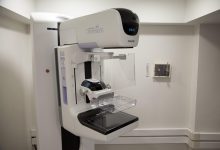 Profissional de saúde ao lado de um equipamento de mamografia em uma unidade hospitalar.