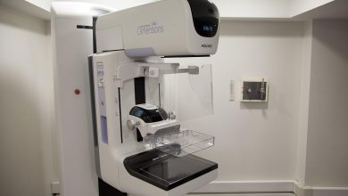 Profissional de saúde ao lado de um equipamento de mamografia em uma unidade hospitalar.