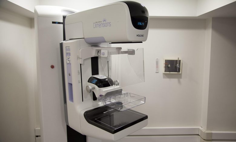 Profissional de saúde ao lado de um equipamento de mamografia em uma unidade hospitalar.